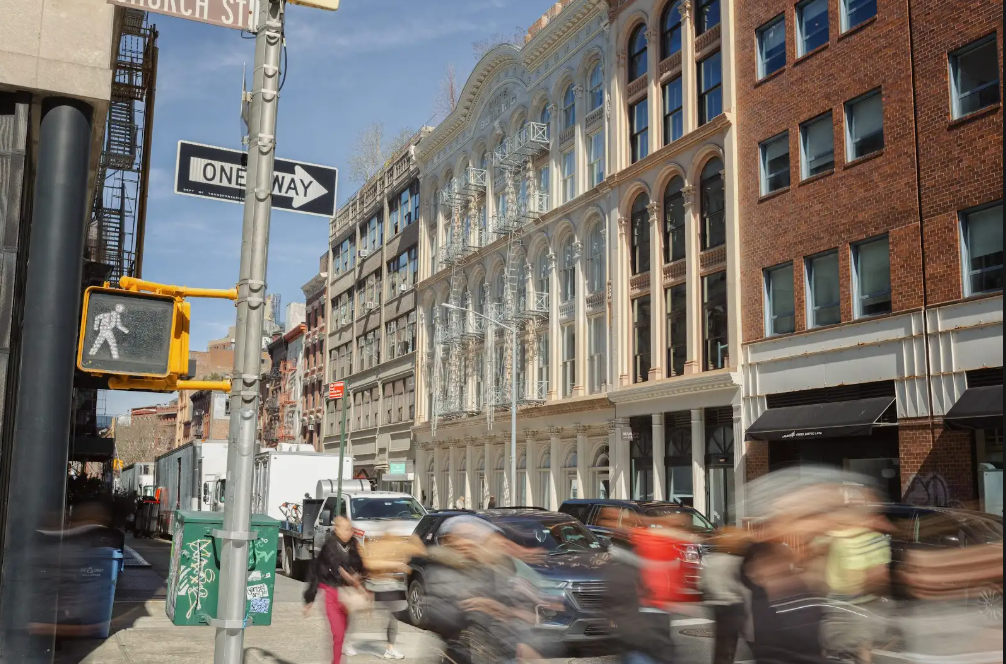 Busy street intersection with blurred pedestrians and traffic, featuring a "One Way" sign and a historic building.