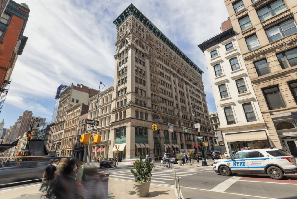 Wide-angle view of a distinctive wedge-shaped building in a bustling city intersection with a police car.